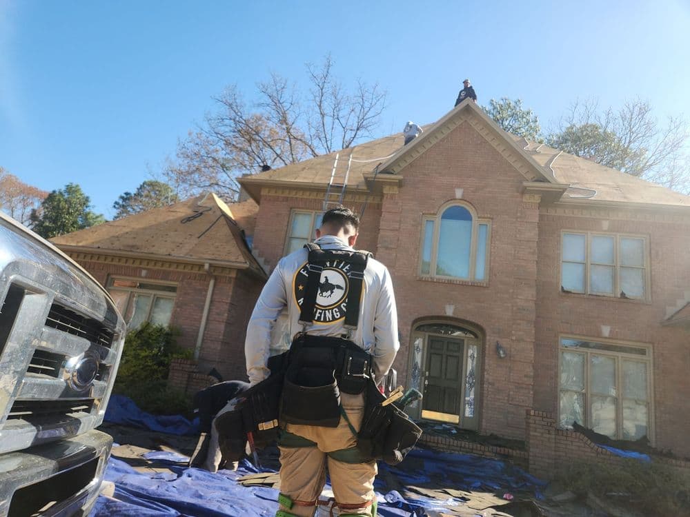 Roofing professional assessing a home's roof with tools, blue tarp, and ladder visible.