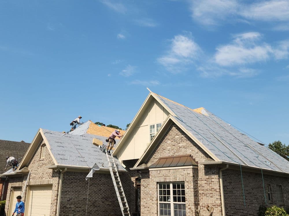 Roofing crew installing new shingles on a residential home under a clear blue sky.