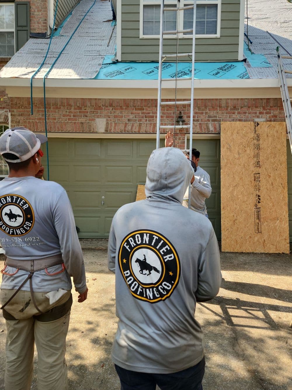 Roofing crew working on home with ladder and safety precautions in progress. Frontier Roofing Co.