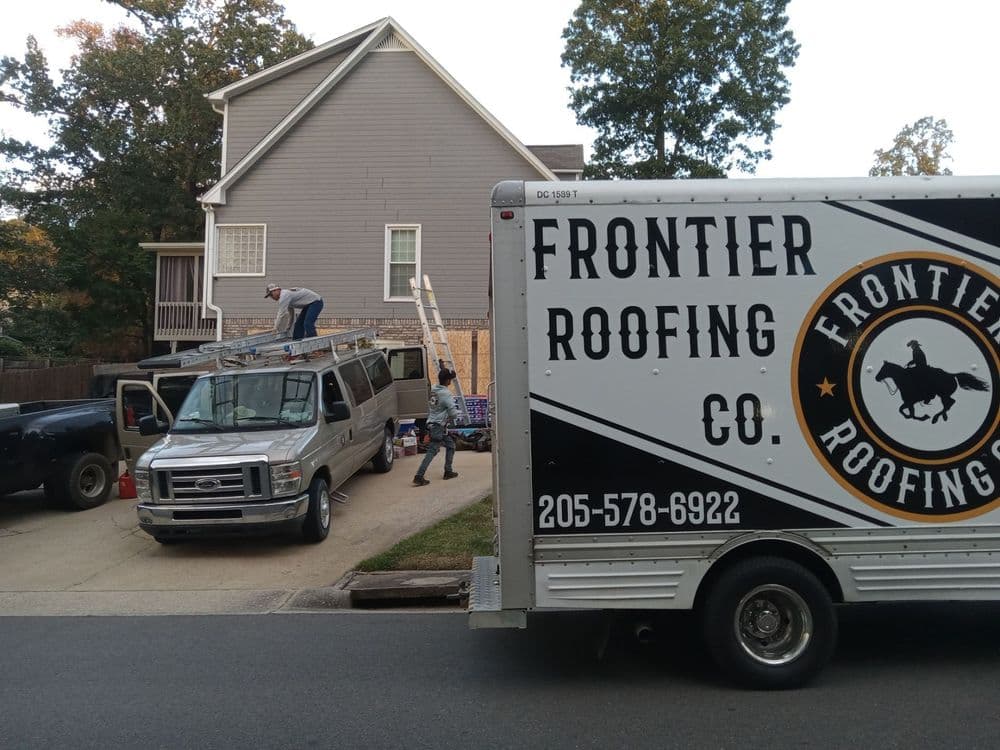 Roofing crew working on a house with a Frontier Roofing Company truck in the foreground.