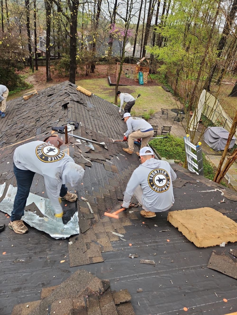 Roofing crew removing old shingles from a residential roof during a repair project.
