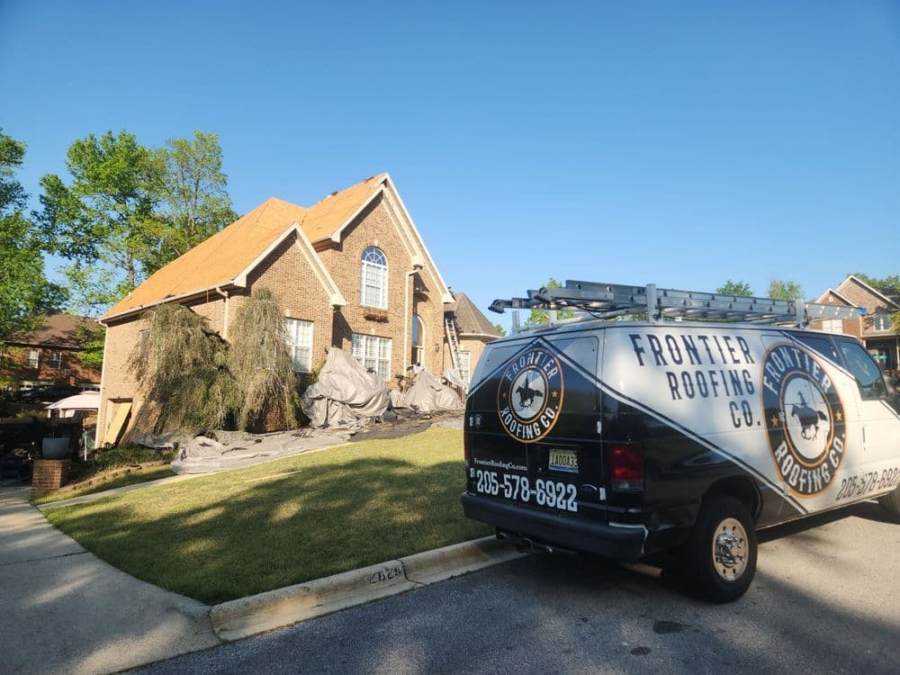 Frontier Roofing van parked by a home undergoing roof replacement with tarps on the lawn.