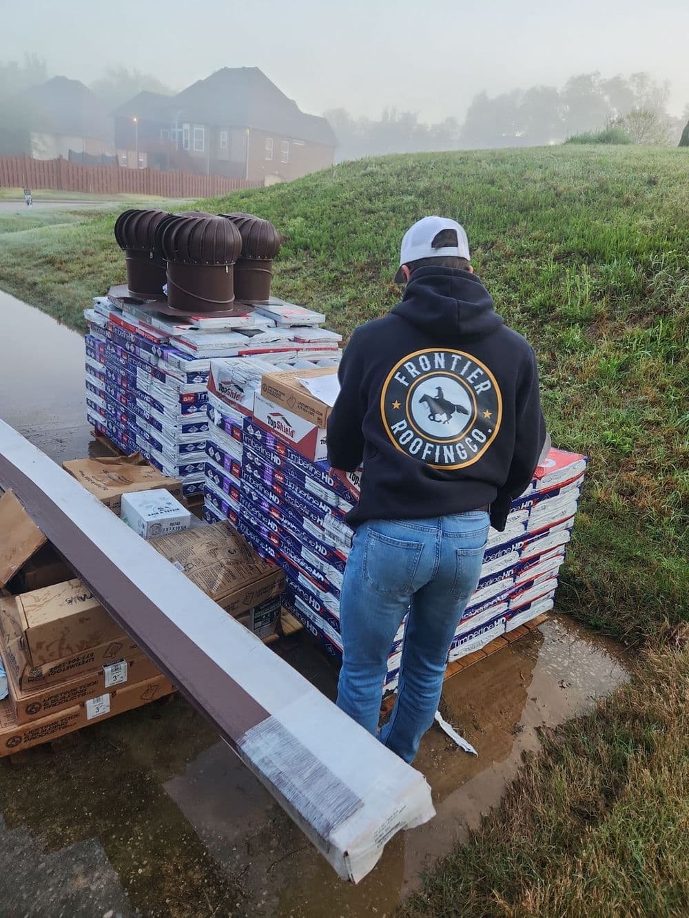 Worker inspecting roofing materials at a construction site in the morning fog.