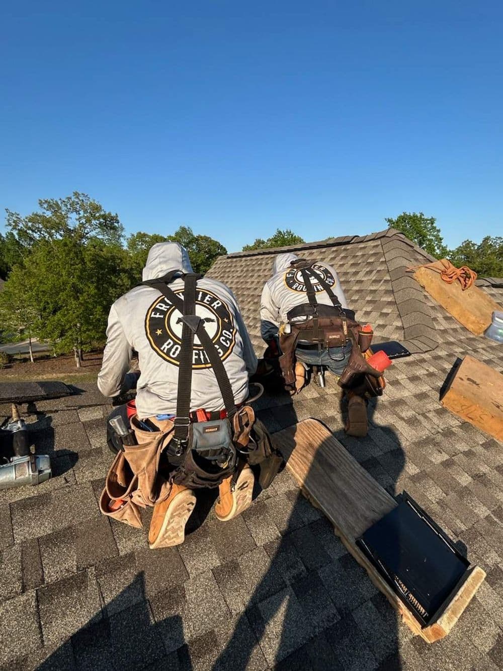 Two roofers working on a residential roof installation under a clear blue sky.
