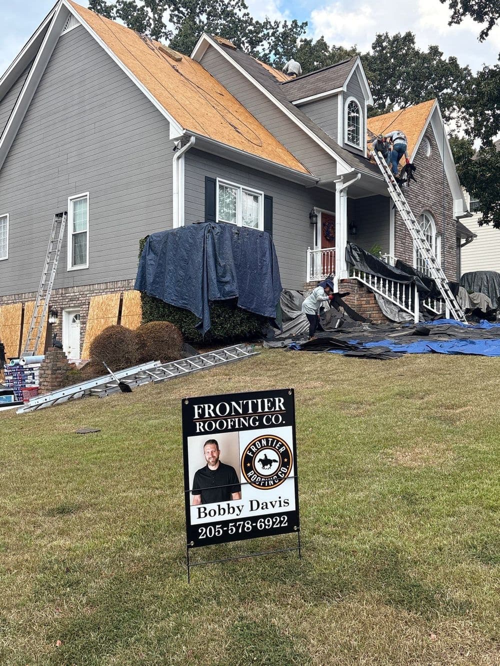 Roofing crew working on a house, featuring a sign for Frontier Roofing Co. and Bobby Davis.