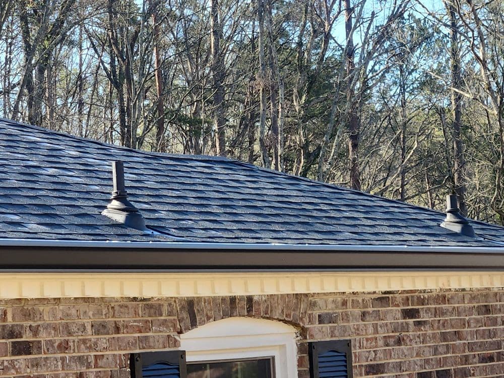 Newly installed gray shingles on a residential roof with metal vents and wooded background.