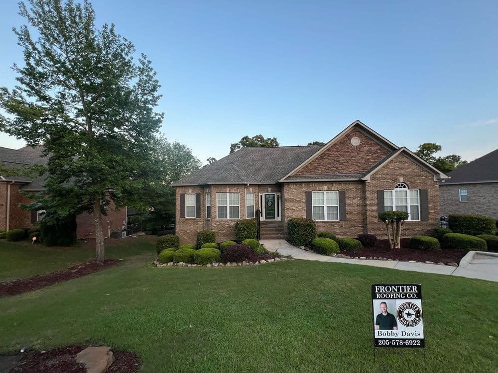 Brick house with landscaped yard and sign for Frontier Roofing Company.