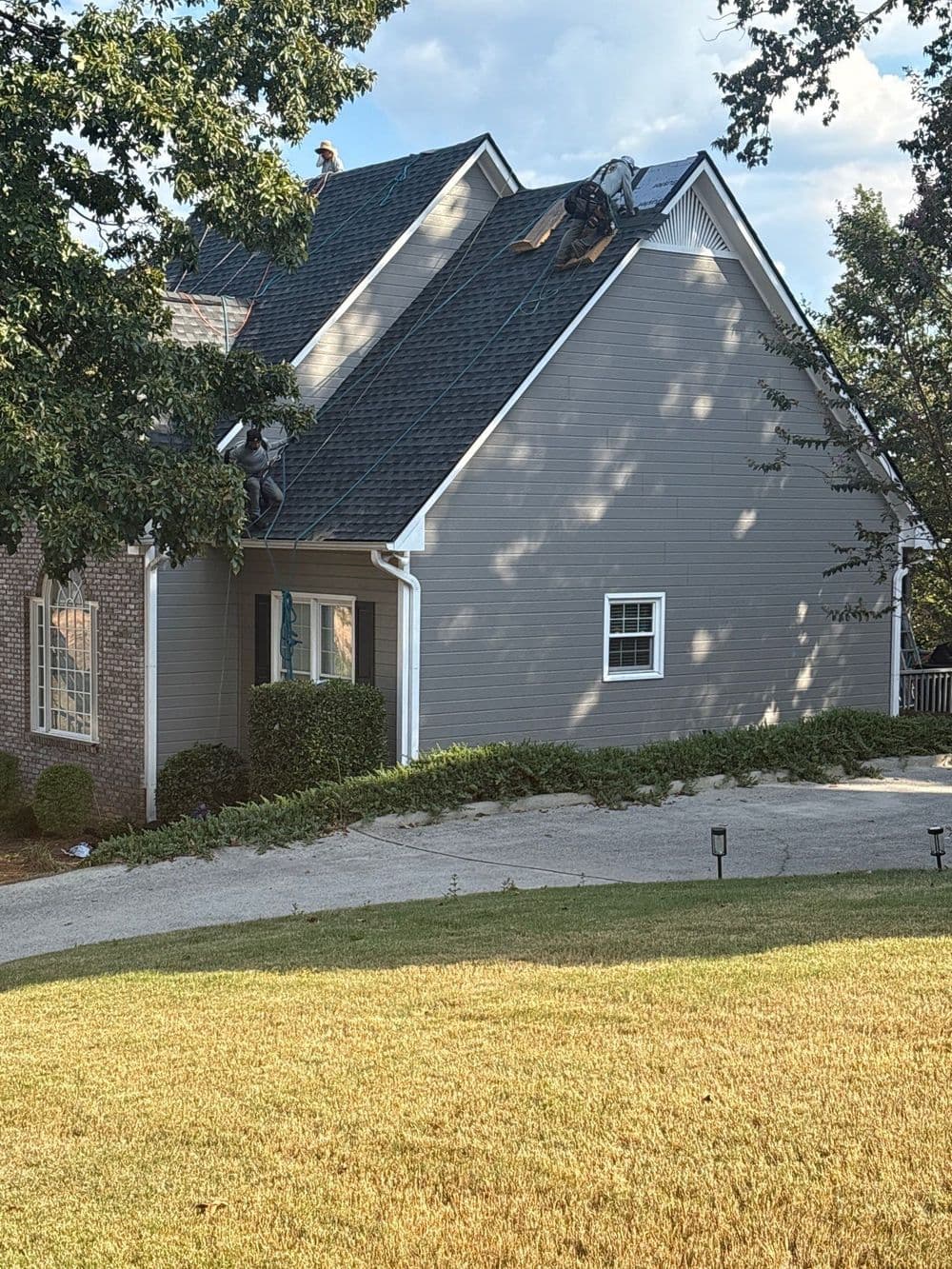 Roofing contractors working on residential house roof under cloudy sky.