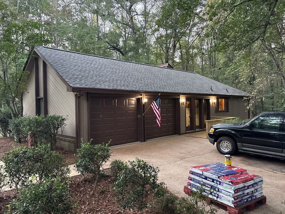 Modern house exterior with a garage, American flag, and landscaping in a wooded area.