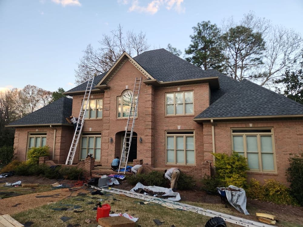 Workers renovating a large brick house with ladders and construction equipment outside.