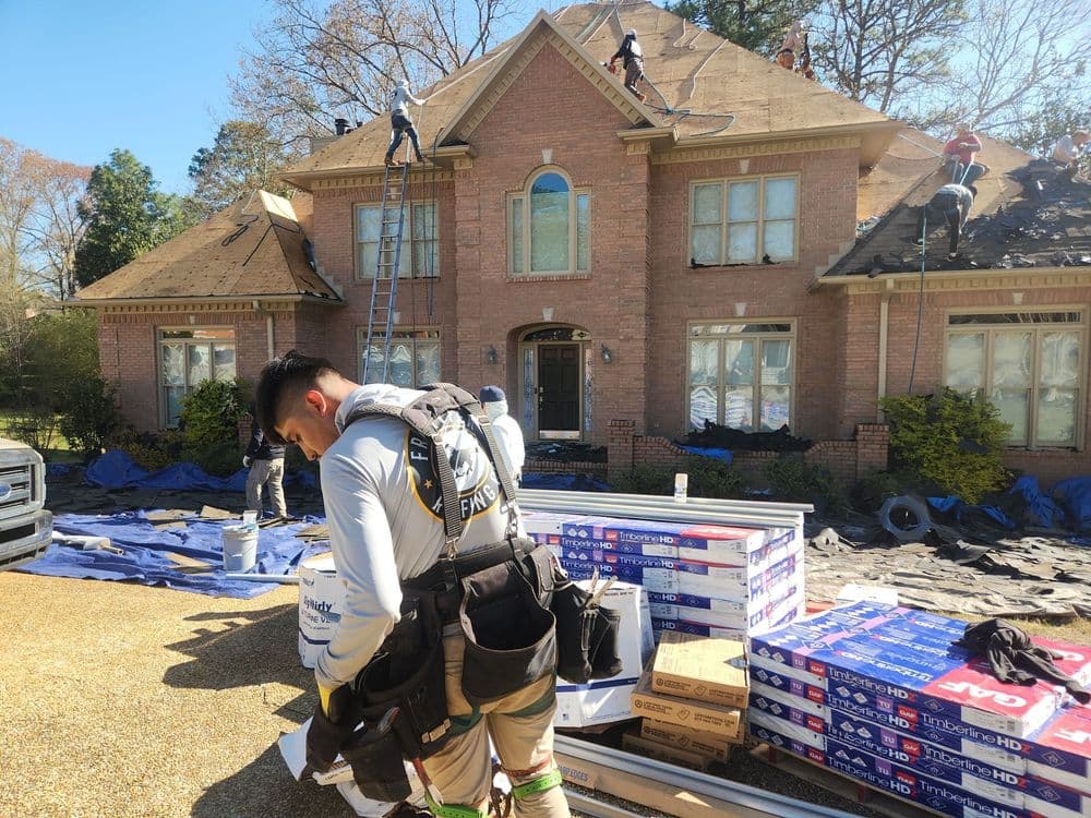 Roofers replacing shingles on a house, with materials and equipment in the foreground.