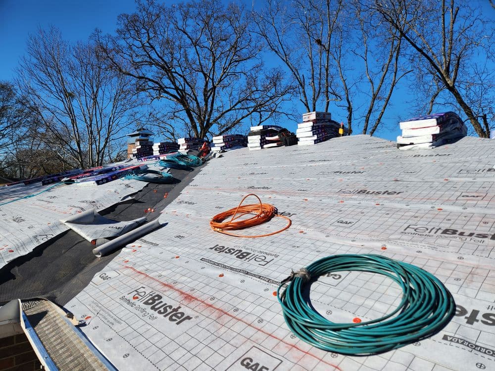 Roofing materials and tools on a sloped roof under a clear blue sky.