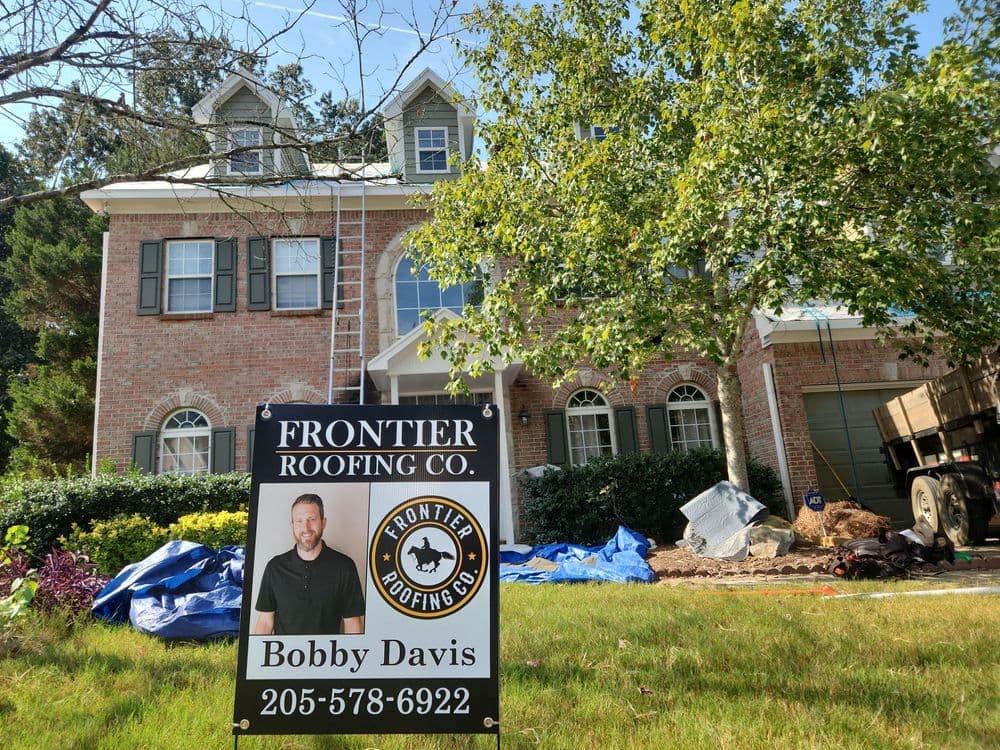 Frontier Roofing Company sign in front of a home with construction materials and a tree.
