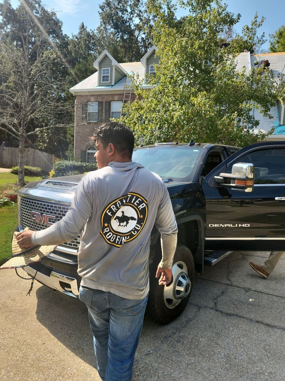 Man wearing a 'Frontier' shirt near a GMC Denali truck in a suburban setting.