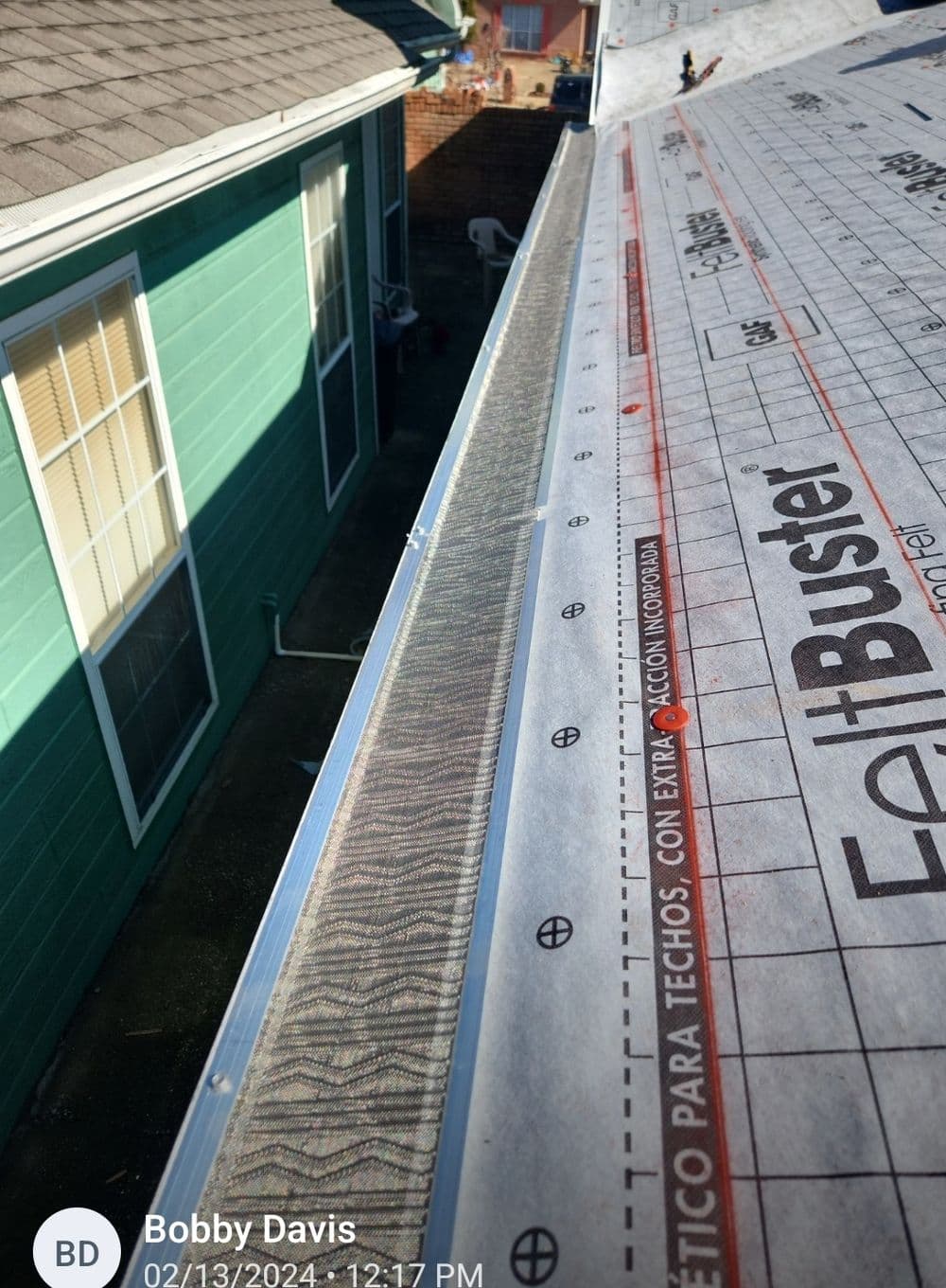 Gutter installation process showing rooftops and adjoining buildings.