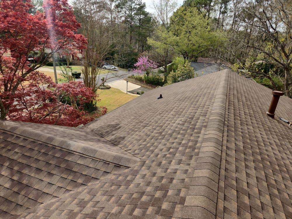 Roofing shingles on a sloped roof with trees and a driveway in the background.