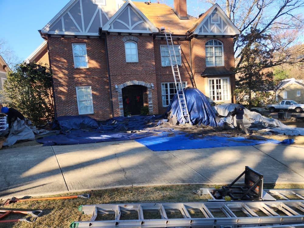 Home undergoing roof repair, with ladders and tarps laid out for protection.