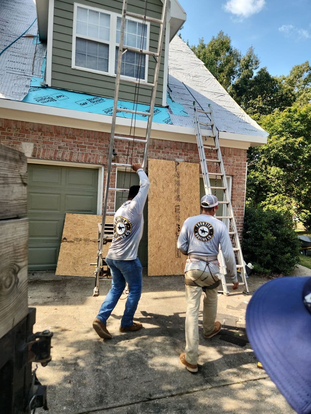 Two workers installing a new roof with ladders at a residential home.