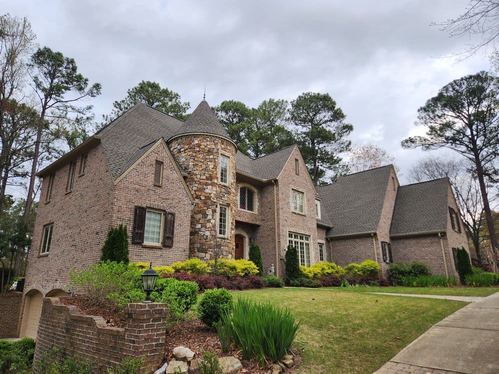 Elegant brick house with stone accents, lush landscaping, and a cloudy sky.