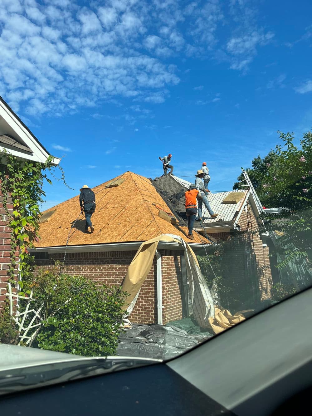 Roofing crew installing shingles on a residential home under a blue sky.
