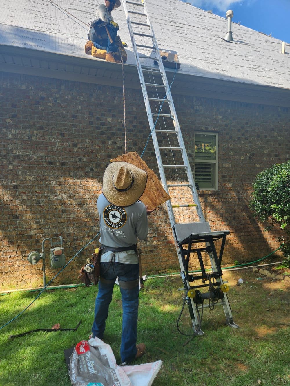 Workers installing insulation on a residential roof using a ladder and tools in a backyard setting.