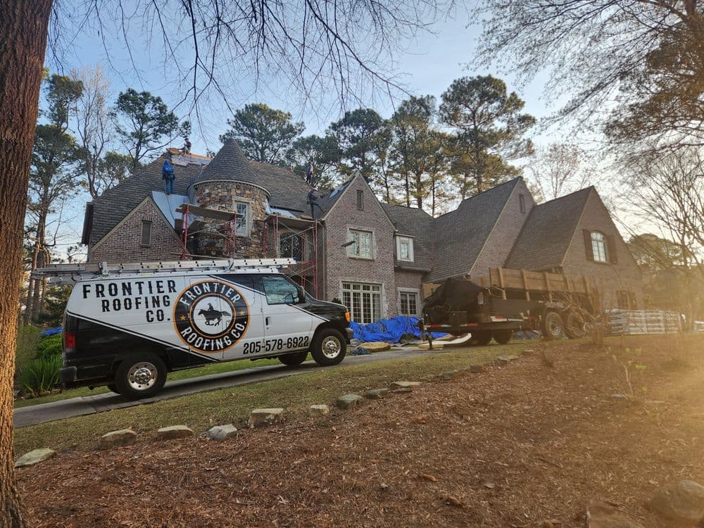 Roofing contractors working on a home with a Frontier Roofing Company van and equipment.
