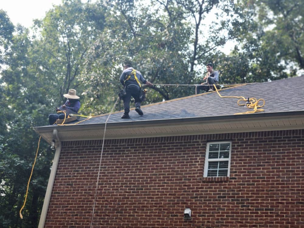 Roofers performing maintenance on a residential roof using safety harnesses and ropes.