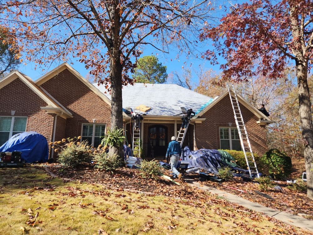 Roofing contractors installing a new roof on a house with trees and autumn leaves.