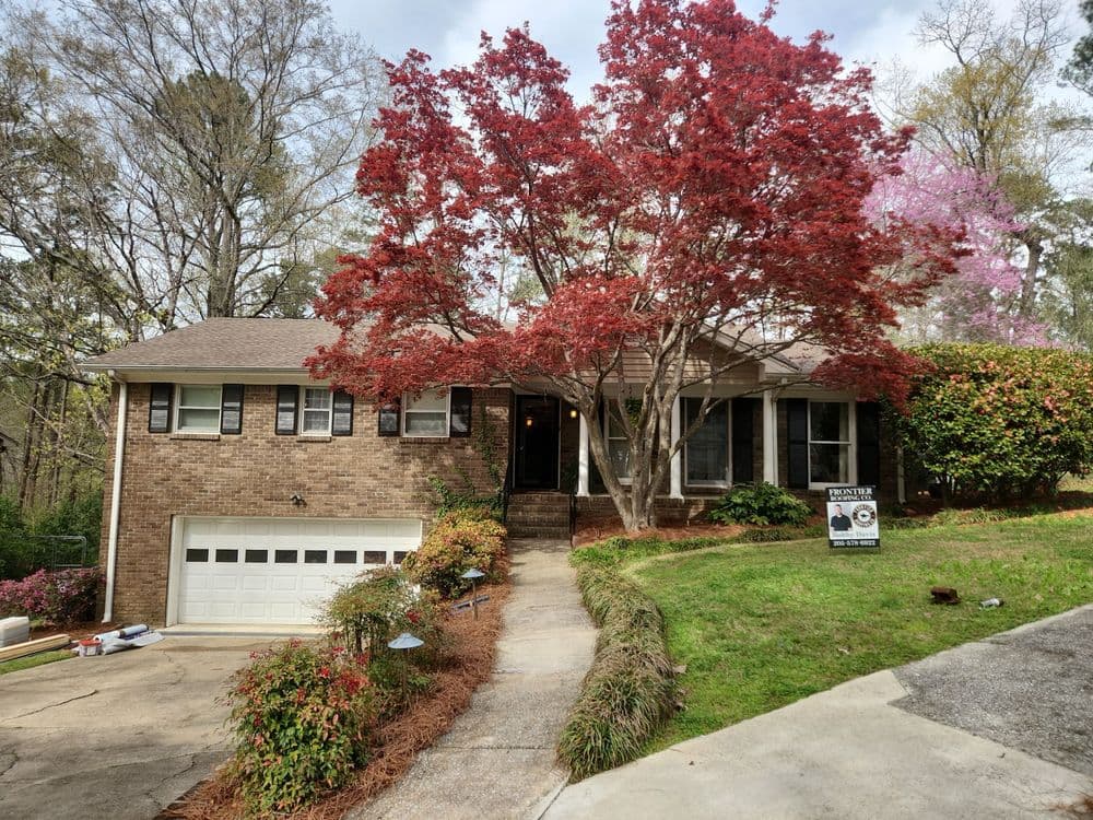 Brick house with red maple tree in front, driveway, and for sale sign in a suburban setting.