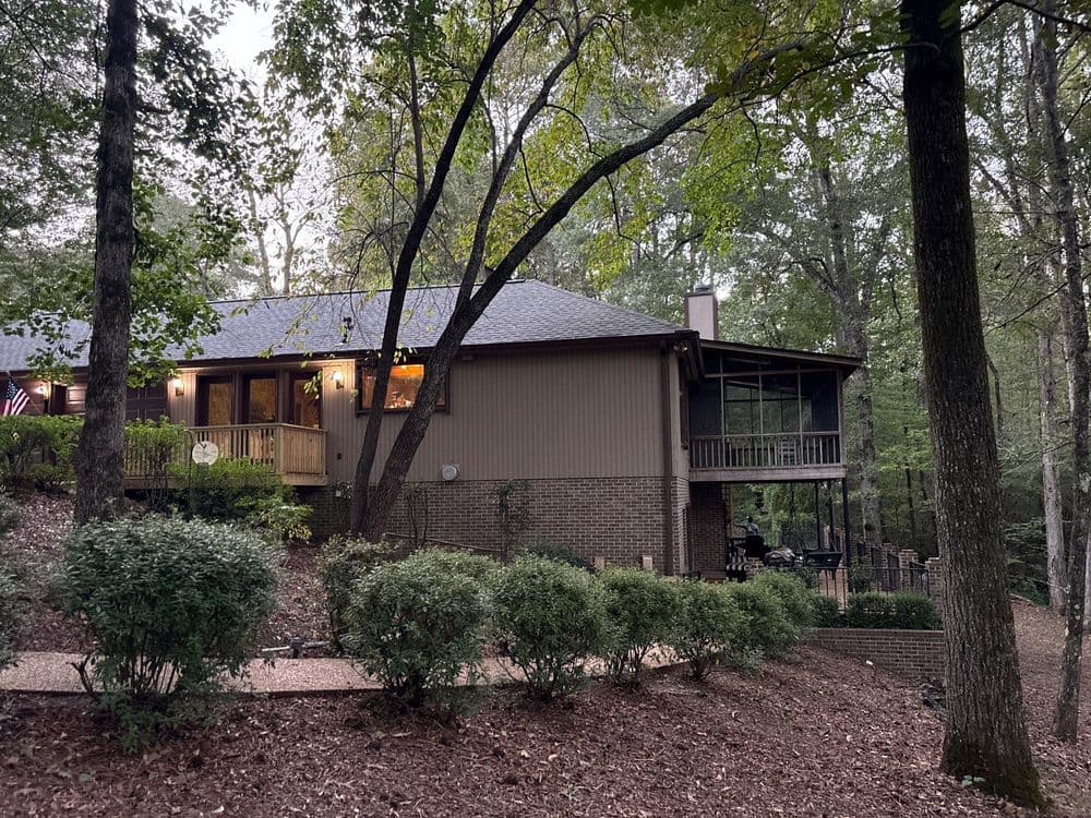 Modern wooden house nestled in a green forest, surrounded by trees and landscaping.