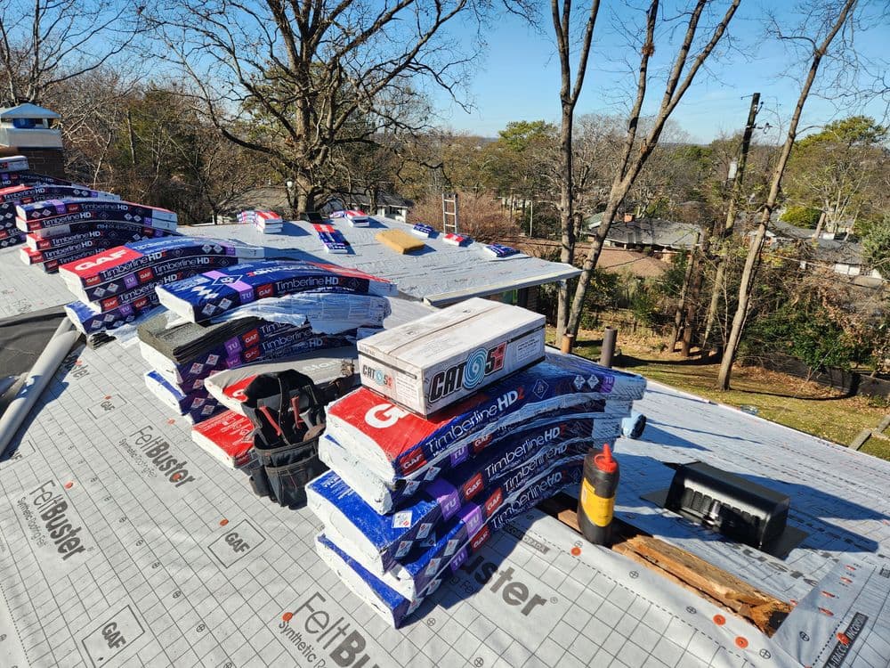 Roofing materials stacked on a sloped roof, including TimberTech HD shingles and tools.
