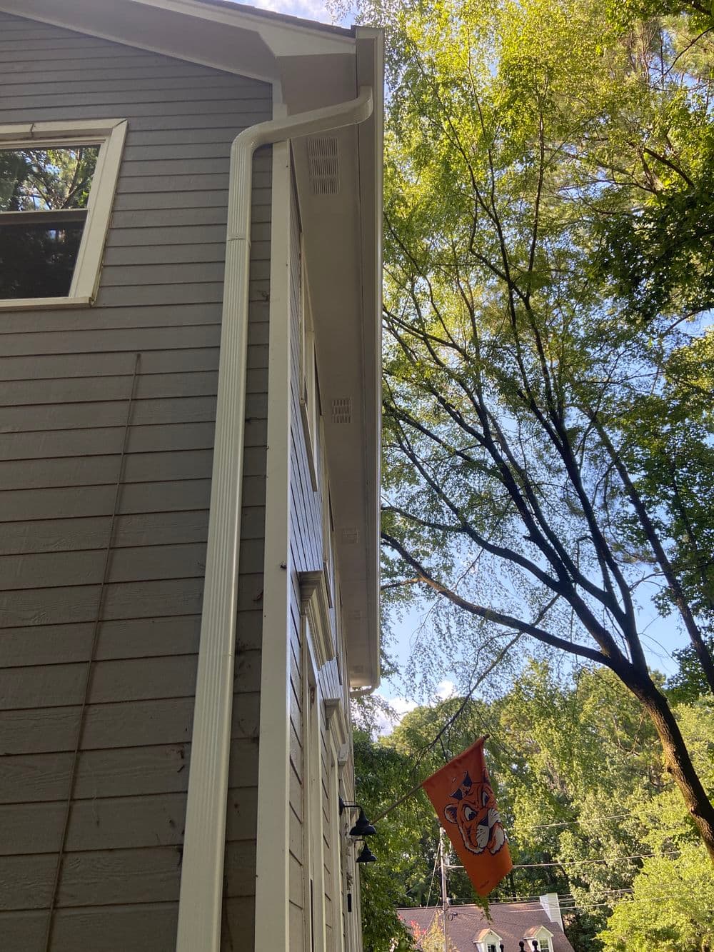 House corner with white gutters and orange flag hanging, surrounded by green trees.
