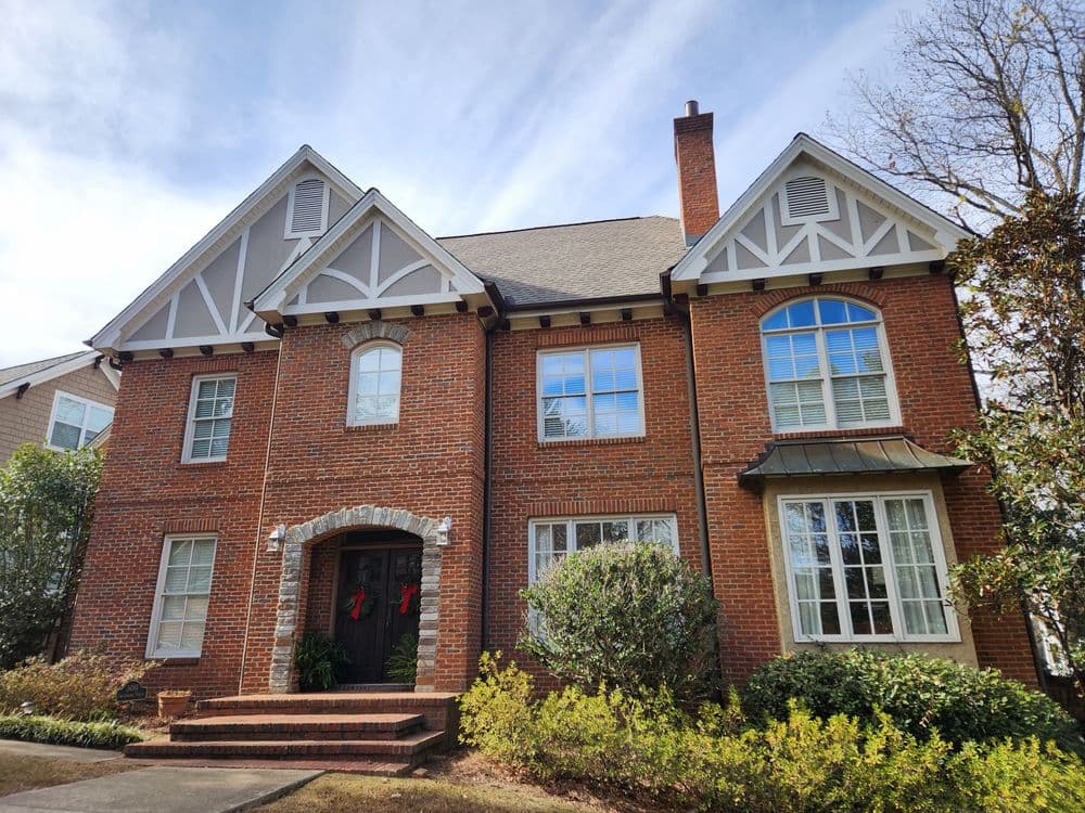Elegant brick home with decorative trim, large windows, and festive holiday wreaths.