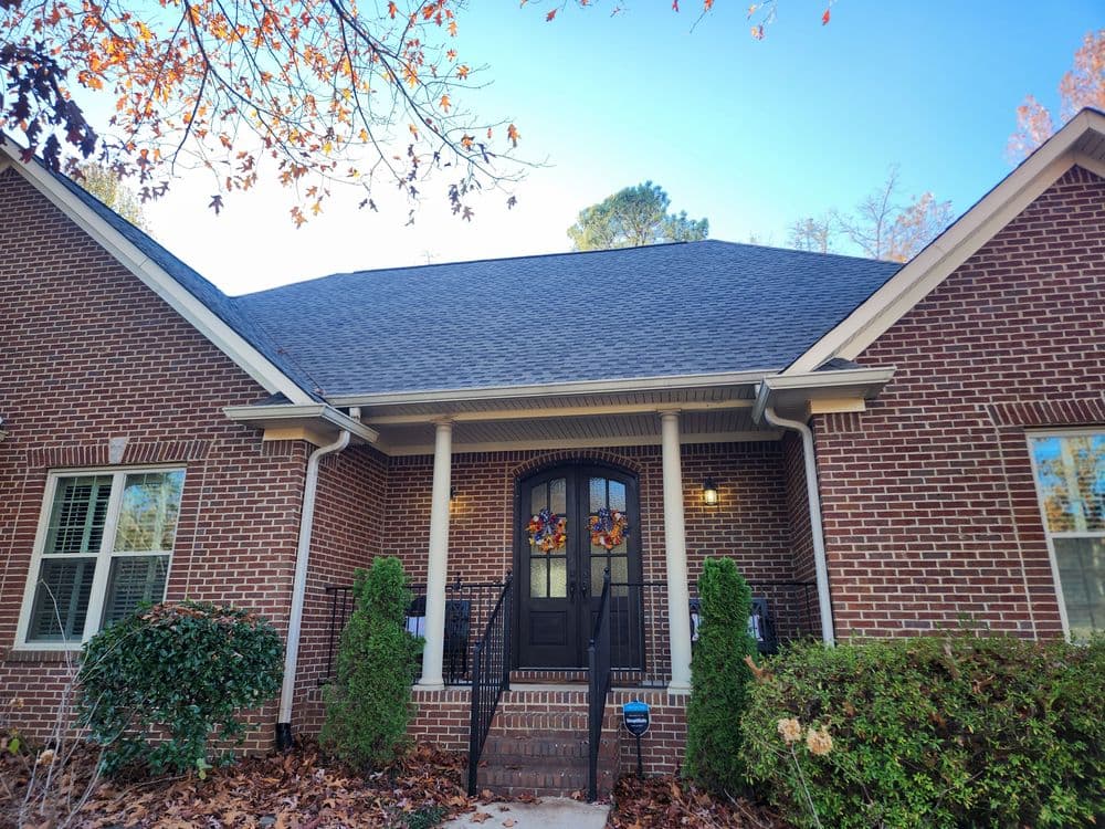 Brick house with a black door, decorative wreath, and lush green landscaping.