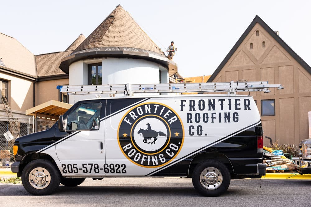 Frontier Roofing Co. van with ladders, parked near a building under renovation.