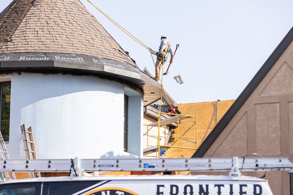 Construction worker installing roofing on a building with a round tower and scaffolding.