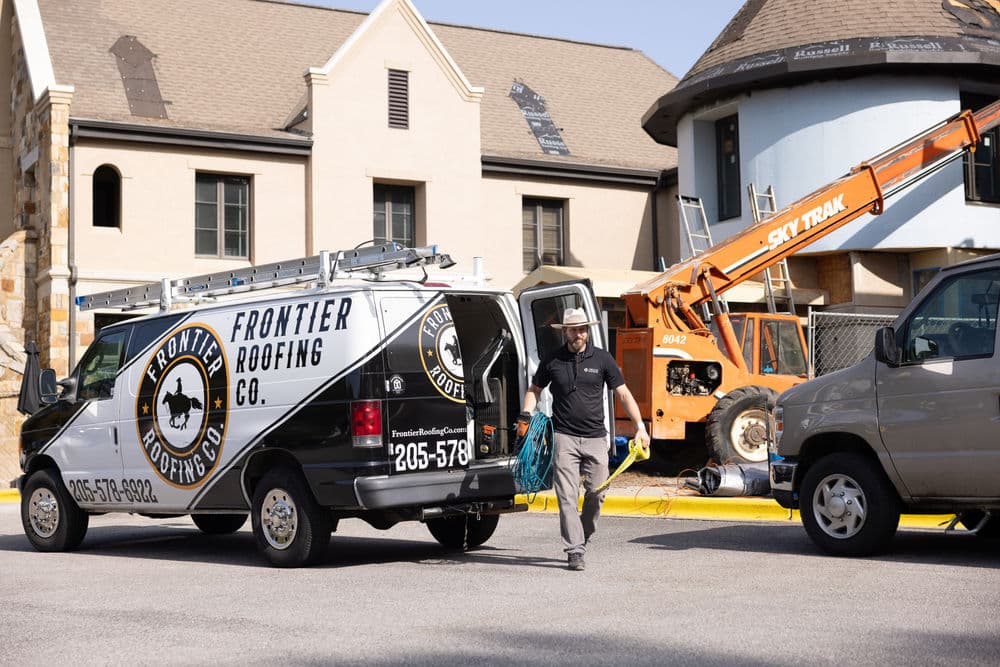 Frontier Roofing Company truck at a construction site with equipment and workers.