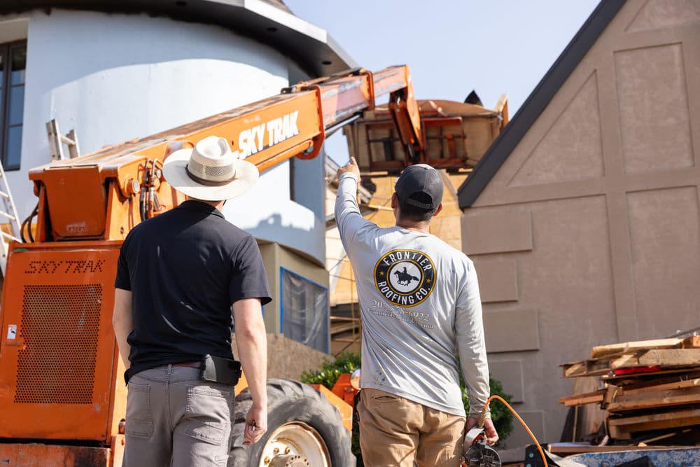 Construction workers operating a Skytrak lift at a building site. Safety gear and tools visible.