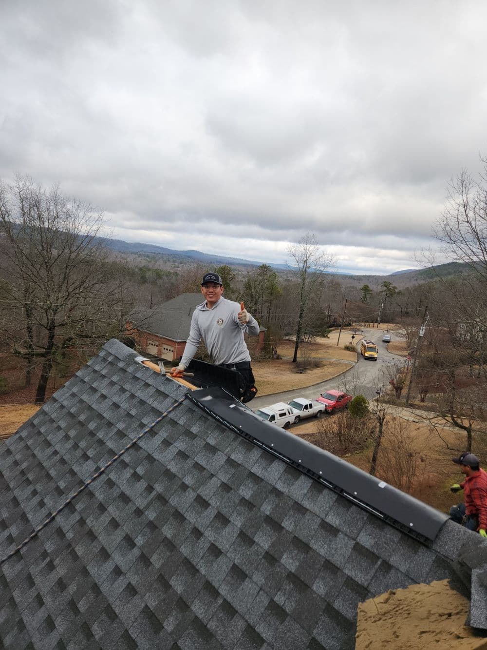 Roofer working on a house roof with scenic view, thumbs up on a cloudy day.