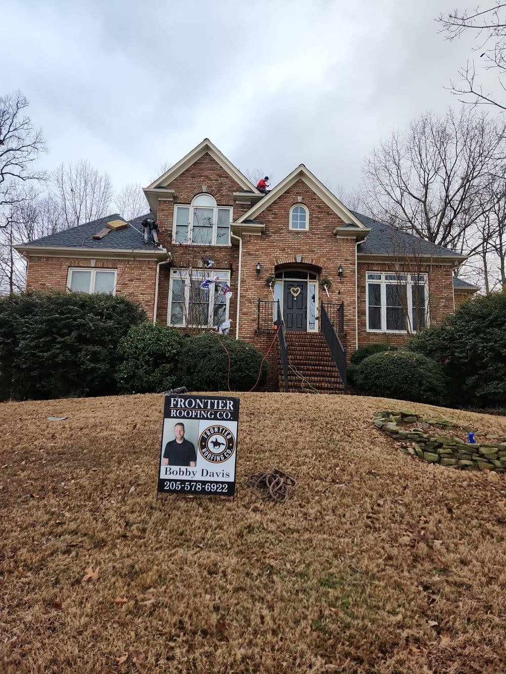 Roof repair work in progress on a brick home with a contractor's sign in front.